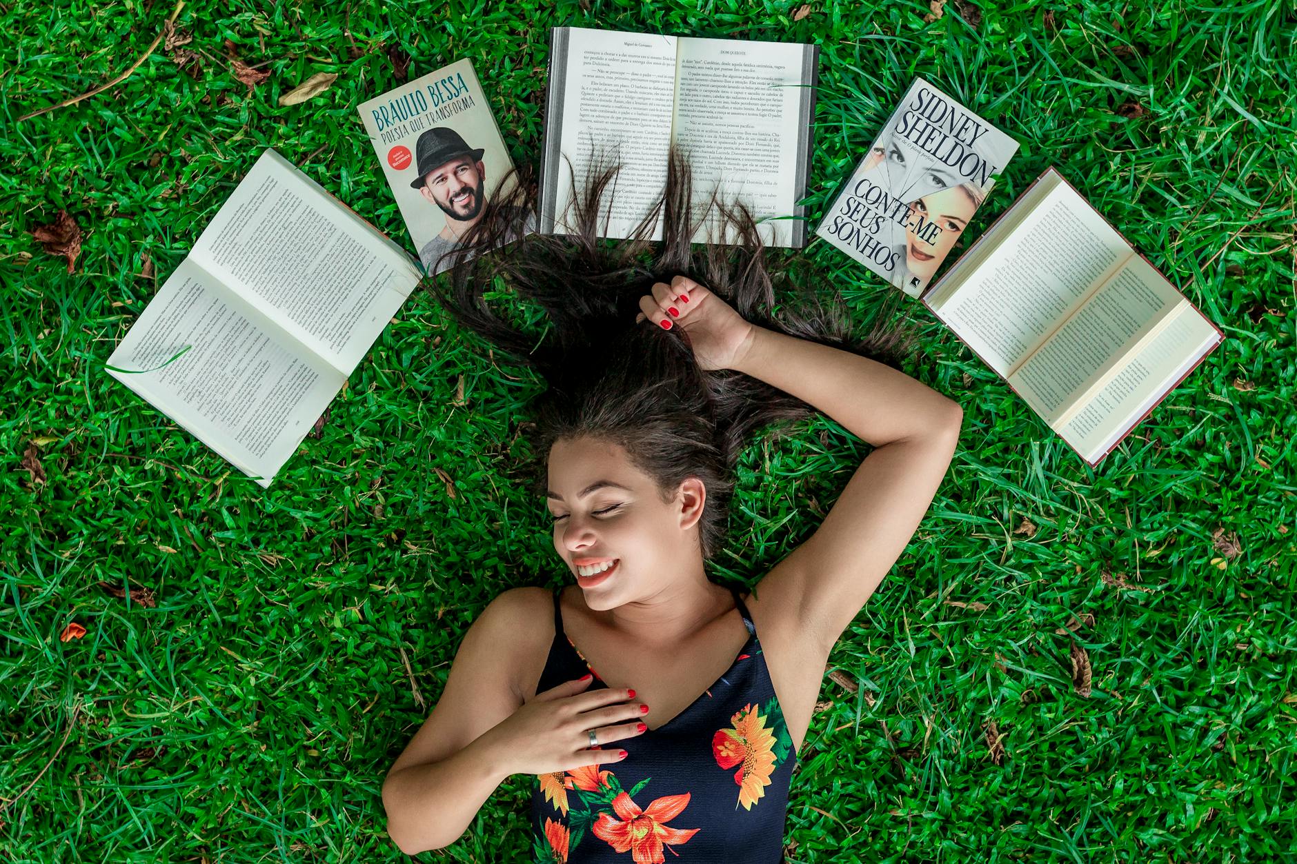 woman lying down on grass beside opened books